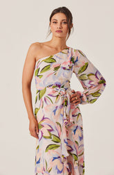 A woman wearing a one-shoulder, long-sleeve dress with a floral print in shades of pink, purple, blue, and green. The dress features a waist tie with a bow.